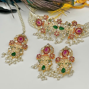 May include: A gold necklace set with a multi-strand pearl chain, a floral pendant with red, green, and white stones, and matching earrings. The necklace and earrings have pearl drops.