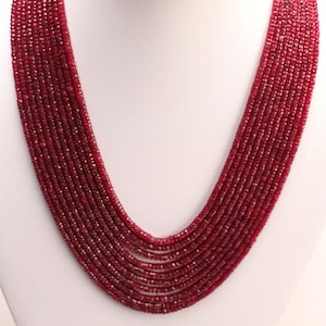 May include: A long, multi-strand necklace made of small, faceted ruby beads. The necklace is displayed on a white mannequin bust.
