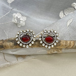 May include: A pair of heart-shaped earrings with a red gemstone centre and a halo of clear rhinestones.