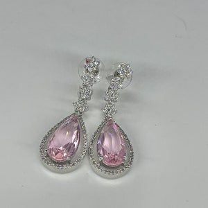 May include: A pair of silver dangle earrings with pink pear-shaped stones and a row of clear cubic zirconia stones.