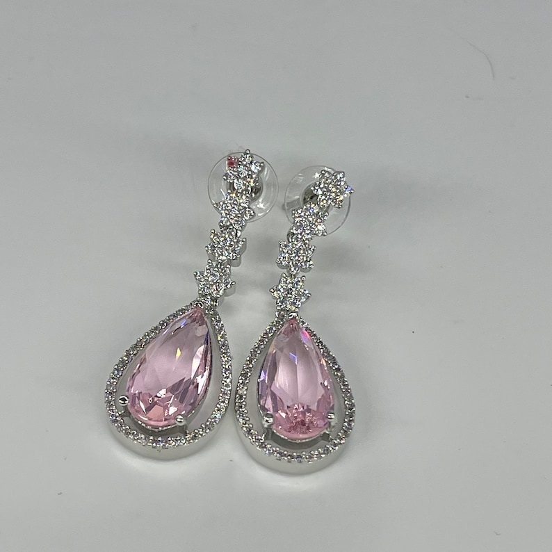 May include: A pair of silver dangle earrings with pink pear-shaped stones and a row of clear cubic zirconia stones.