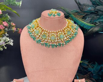 Op de afbeelding: Een groene en gouden kettingset met een grote, traanvormige hanger. De ketting is versierd met kleinere groene stenen en parels. De oorbellen zijn ook groen en goud, met bijpassende traanvormige hangers.