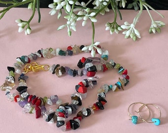 May include: A multi-colored gemstone necklace with a gold clasp and two turquoise hoop earrings. The necklace is made of small, irregular shaped stones in shades of red, black, white, green, blue, and purple.