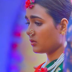 May include: A woman wearing traditional Indian jewelry, including a nose ring and a pearl necklace. She has a red flower in her hair and is wearing a green and red sari.
