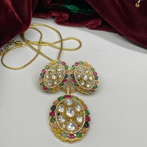 Peut inclure: Un collier en or avec un pendentif et des boucles d'oreilles. Le pendentif et les boucles d'oreilles sont de forme ovale et présentent un motif de pierres blanches entourées de pierres colorées.