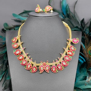 May include: A gold necklace featuring a chain and a pendant crafted from numerous pink and green stones. The pendant is teardrop-shaped and embellished with tiny, glittering stones. The necklace is presented on a black mannequin.