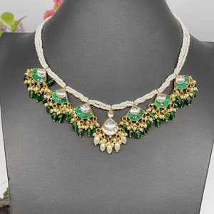 May include: A white pearl necklace with green and white gemstone pendants. The necklace has a layered design with multiple strands of pearls.