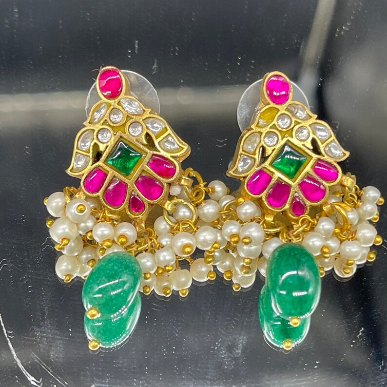 May include: Gold-toned earrings with a floral design, featuring pink and green gemstones, white pearls, and a dangling green stone. The earrings have a detailed, ornate appearance, with a classic, elegant style.