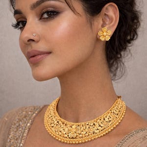 May include: A gold-toned necklace featuring an intricate floral and leaf pattern with a beaded border, paired with matching five-petaled flower stud earrings. The jewelry set displays a textured, matte finish with detailed metalwork throughout the pieces.