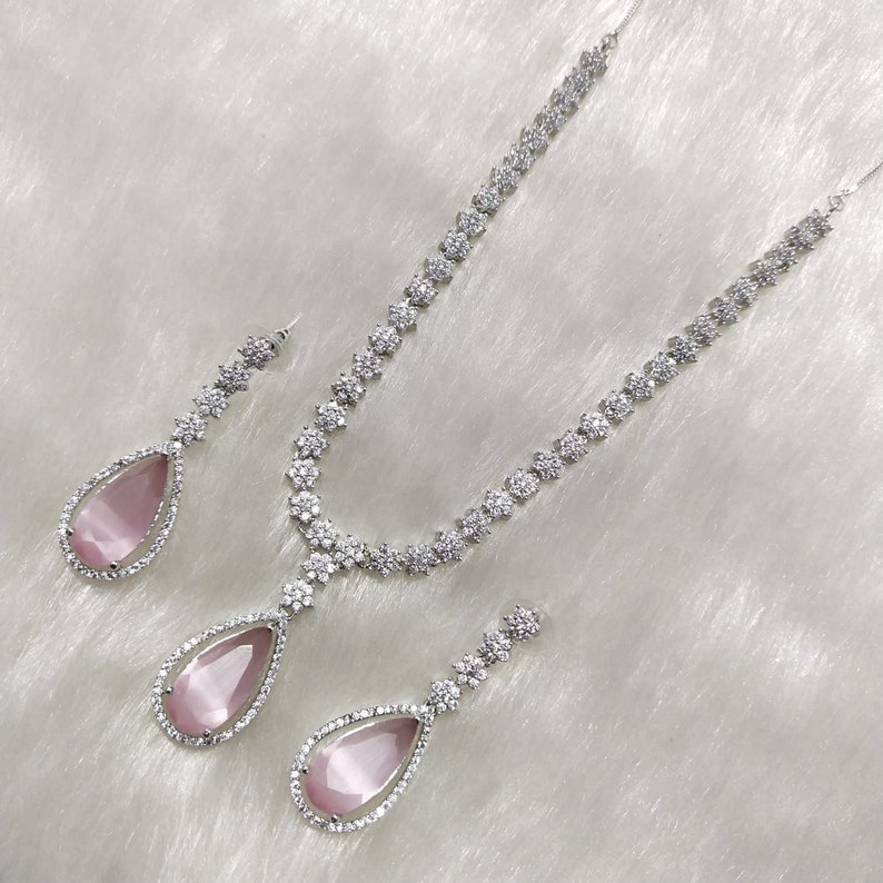May include: A silver necklace and earrings set with a teardrop-shaped pink stone surrounded by clear cubic zirconia stones.