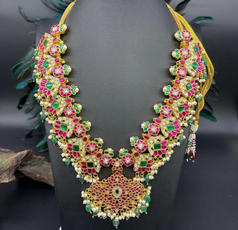 May include: A gold necklace with a pink and green gemstone design. The necklace has a pendant in the shape of a flower with a pink center and green petals.