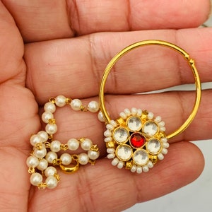 May include: Gold nose ring with a red stone and white pearls. The ring has a chain of white pearls attached to it.
