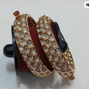 May include: Two gold-toned bangles with a honeycomb pattern of clear stones. The bangles are displayed on a black stand with a red velvet interior. The text "No 455" is in the upper right corner.