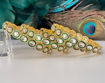 Op de afbeelding: Drie gouden armbanden met groene emaille en witte ovale stenen. De armbanden zijn op elkaar gestapeld.