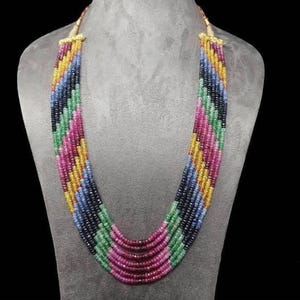 Peut inclure: Un collier à plusieurs rangs aux couleurs vives, composé de perles roses, vertes, jaunes, bleues et noires. Le collier est présenté sur un buste gris, mettant en valeur son design en couches et son travail de perles complexe. Un bijou remarquable.