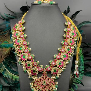 May include: A gold necklace with pink and green gemstones, a matching pair of earrings with pink and green gemstones, and a gold chain with a tassel.