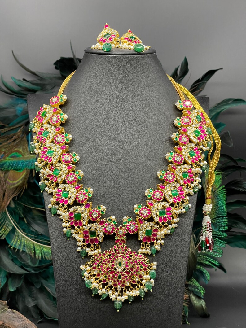 May include: A gold necklace with pink and green gemstones, a matching pair of earrings with pink and green gemstones, and a gold chain with a tassel.