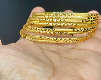 May include: A set of eight gold bangles with a textured surface. The bangles are stacked on top of each other.