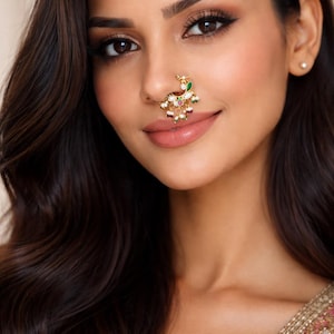 Op de afbeelding: Een goudkleurige neusring met een pauwontwerp, versierd met groene, witte en rode edelstenen. Het sieraad wordt op de neus gedragen en toont ingewikkelde details en levendige kleuren. Deze etnische sieraden voegen elegantie toe.