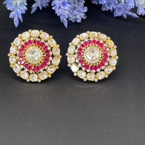 Può includere: Un paio di orecchini rotondi in oro con un design circolare di pietre preziose bianche e rosa. Gli orecchini hanno una pietra preziosa bianca rotonda centrale circondata da pietre preziose bianche più piccole e un anello di pietre preziose rosa.