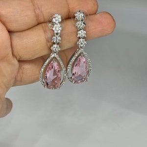 May include: A pair of silver dangle earrings with pink pear-shaped stones and clear crystal accents.