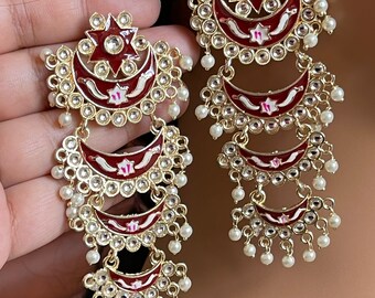 May include: A pair of long, dangling earrings with multiple tiers of crescent moon shapes. Each tier is decorated with white and pink enamel, rhinestones, and pearl accents. The earrings are a burgundy red color.