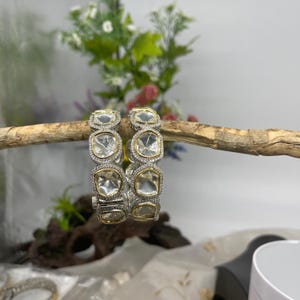 May include: Two silver bangles with clear, faceted stones set in gold. The bangles are stacked on top of each other.