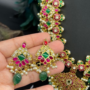 May include: A gold necklace with pink and green gemstones, pearls, and a matching pair of earrings. The necklace has a geometric design with square and rectangular shapes.