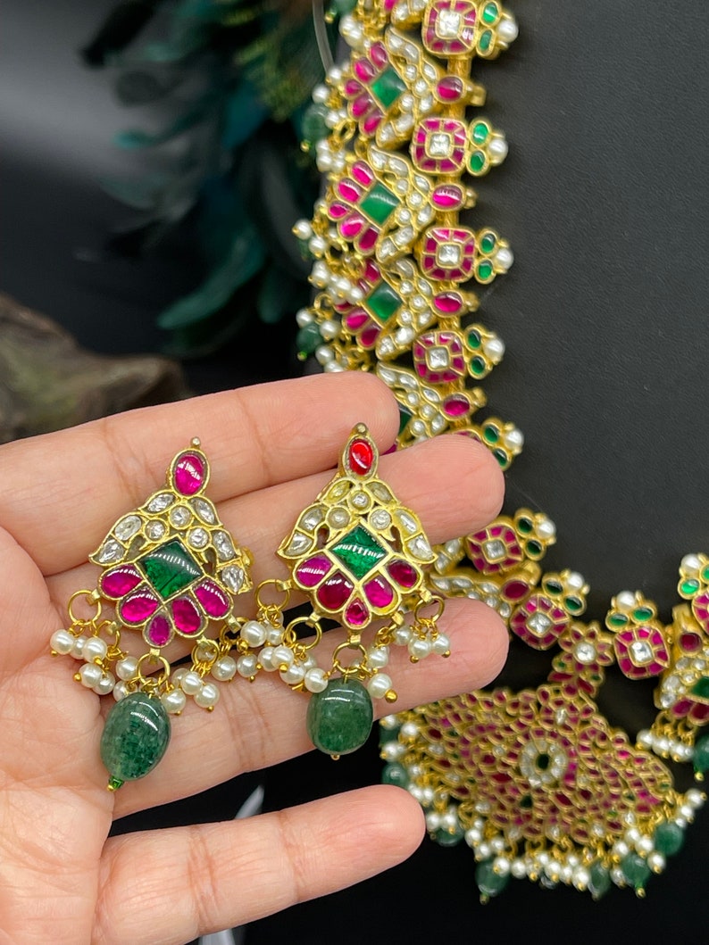 May include: A gold necklace with pink and green gemstones, pearls, and a matching pair of earrings. The necklace has a geometric design with square and rectangular shapes.