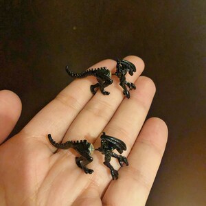 May include: A pair of black alien creature earrings. The earrings are made of metal and have a detailed design.