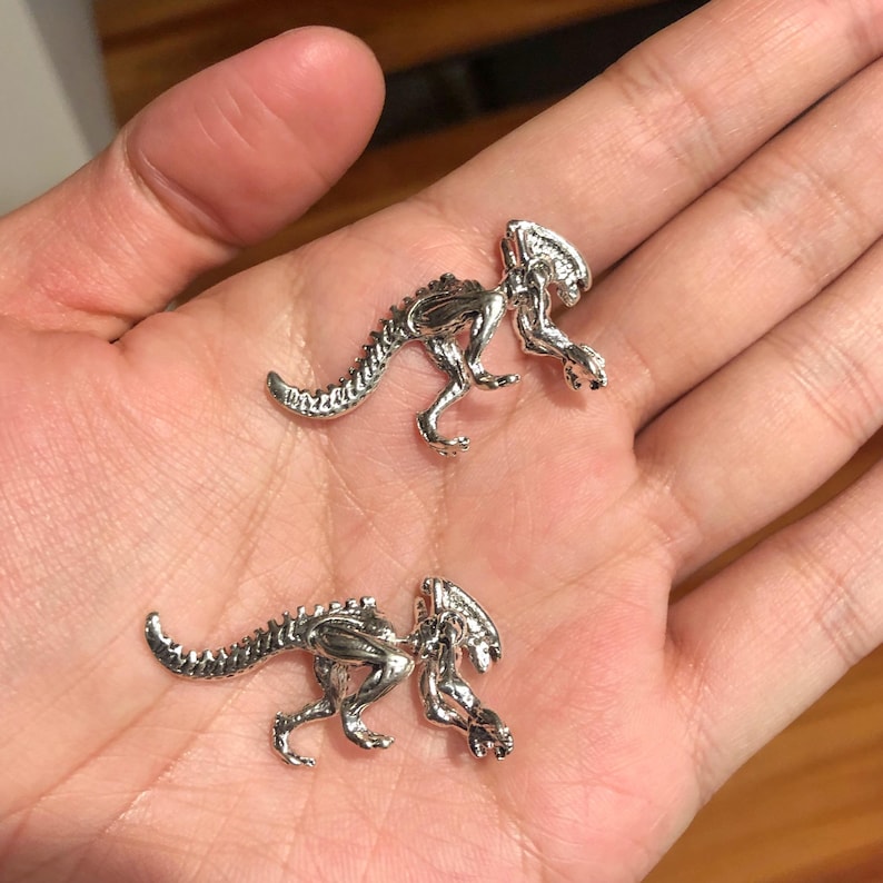 May include: Two silver-colored alien creature figurines. The figurines are detailed and have a textured surface.