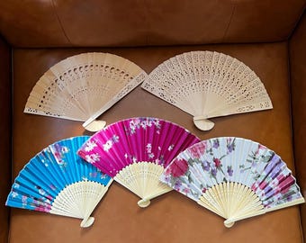 May include: Five hand fans, two made of wood and three made of fabric. The wooden fans are plain and the fabric fans have floral patterns. The fabric fans are blue, pink, and white.