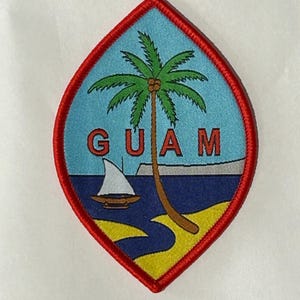 May include: An embroidered patch shaped like a pointed oval with a red border. The design features a light blue sky, a palm tree, a small sailboat on dark blue water, and a yellow sandy shore. The word GUAM is stitched in red capital letters.