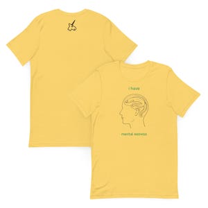 May include: A yellow short-sleeve t-shirt featuring a black line drawing of a human head with an eel inside. The text "i have" and "mental eelness" is printed in green. The back of the shirt displays a small black line drawing of a unicorn.