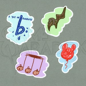 May include: Four colorful stickers with different designs. The first sticker is blue and white with a musical note and the text "I trip on surfaces". The second sticker is green with a brown sloth hanging from a branch. The third sticker is purple with three potatoes hanging from a musical note. The fourth sticker is blue with a red balloon shaped like a hand giving the rock and roll sign.