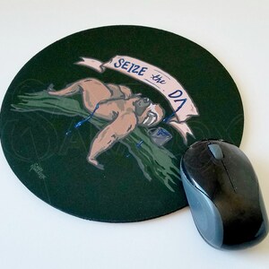 May include: A round black mouse pad with a green background and a cartoon sloth holding a paint bucket. The sloth is on a branch with blue paint dripping from it. The text "SEIZE the DAY" is written on a white banner above the sloth.