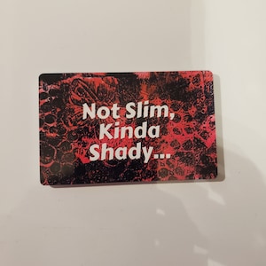May include: A red and black card with the text "Not Slim, Kinda Shady..." printed in white.