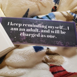 May include: A black and purple bookmark with the text "I keep reminding myself... I am an adult, and will be charged as one."