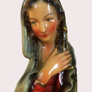 Puede incluir: Un busto vintage de la Virgen María, pintado en tonos de verde, rojo y dorado. El busto está hecho de yeso y tiene una cara detallada con una expresión suave.