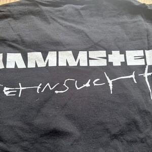 May include: Black t-shirt with the band name "RAMMSTEIN" in large, white, block letters across the top. Below, in a handwritten style, is the phrase "SEHNSUCHT". The shirt is slightly wrinkled.