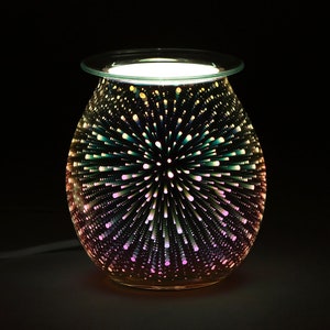 May include: A round glass essential oil diffuser with a starburst pattern in shades of pink, blue, and green. The diffuser is lit and glowing.