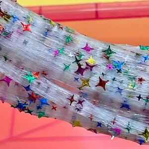 May include: White slime with iridescent star-shaped glitter. The slime is stretched and folded, showing its texture.