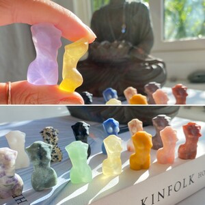 May include: A collection of small, hand-carved figurines made from various types of stone. The figurines are in various colours, including purple, yellow, green, and brown. They are arranged in a row on a table.
