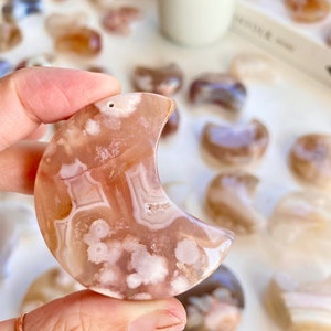 May include: A crescent moon shaped agate carving with a pink and white pattern. The agate has a natural, organic look with a smooth, polished finish.
