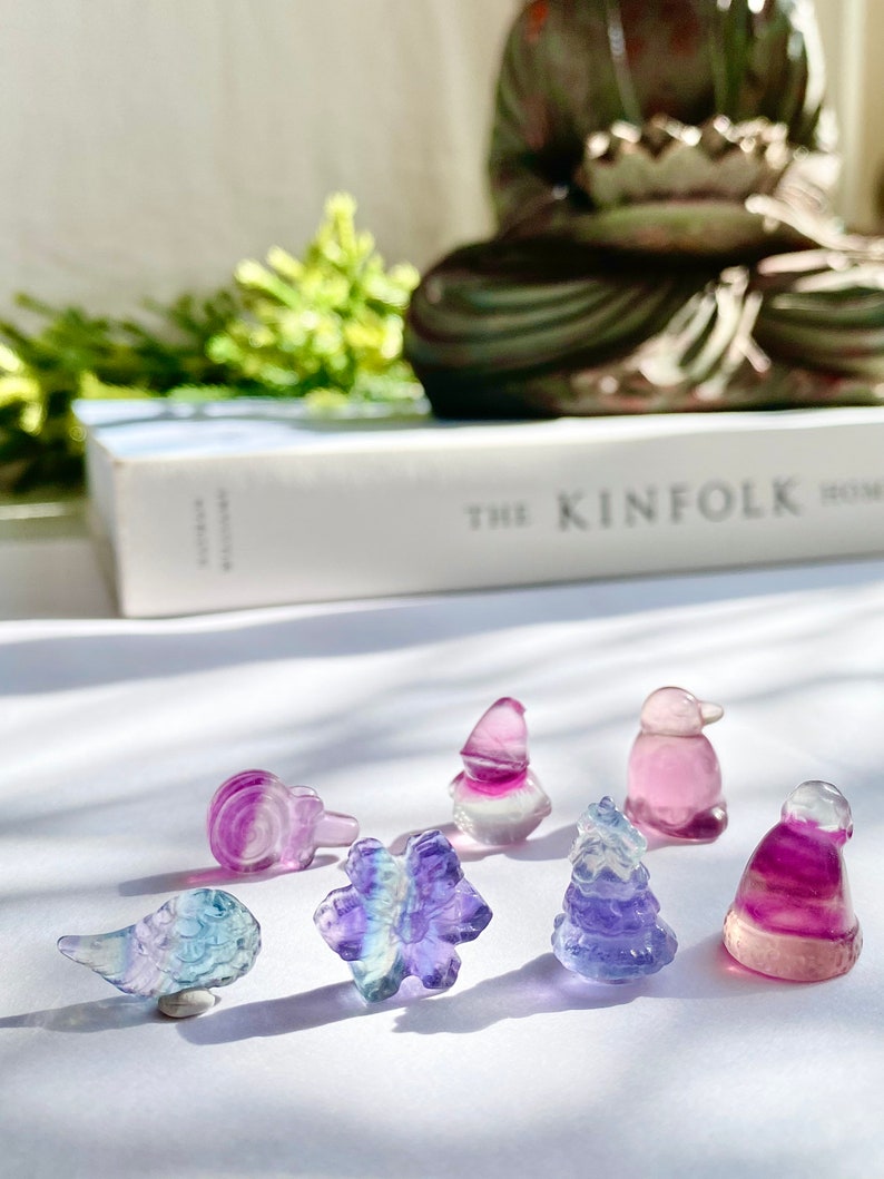 May include: A collection of seven small, colorful, crystal figurines in the shapes of a bird, a flower, a tree, a hat, a penguin, and a gnome. The figurines are made of fluorite, a type of crystal known for its iridescent colors.