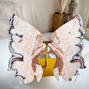 May include: A white, brown, and black butterfly-shaped agate sculpture on a gold stand. The agate has a swirling pattern and is polished to a smooth finish.
