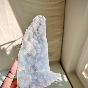 May include: A large, light purple and white crystal with a rough, textured surface. The crystal has a unique, pointed shape and is reminiscent of a mountain range.