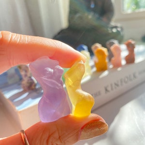 May include: Two small, hand-shaped figurines made of clear glass. One is purple and the other is yellow.