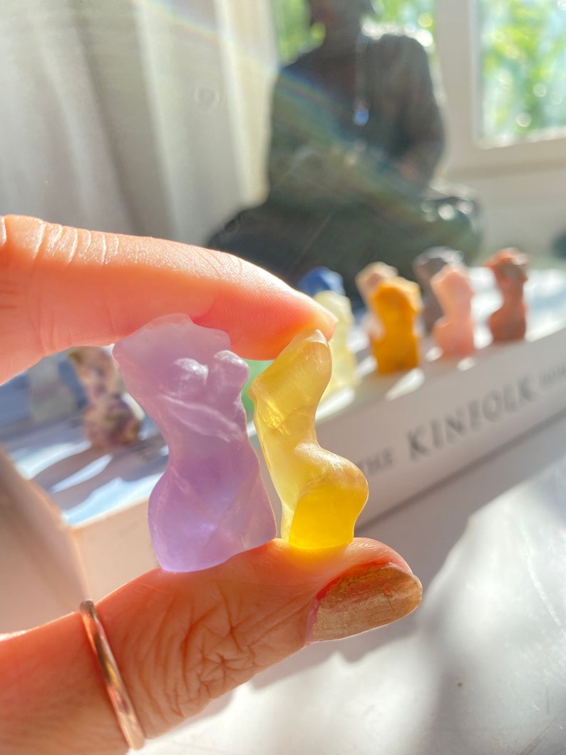 May include: Two small, hand-shaped figurines made of clear glass. One is purple and the other is yellow.