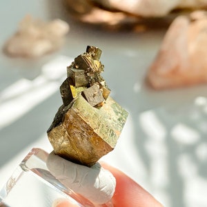 May include: A cluster of gold pyrite crystals with a cubic shape. The crystals are arranged in a pyramid shape and have a metallic sheen.